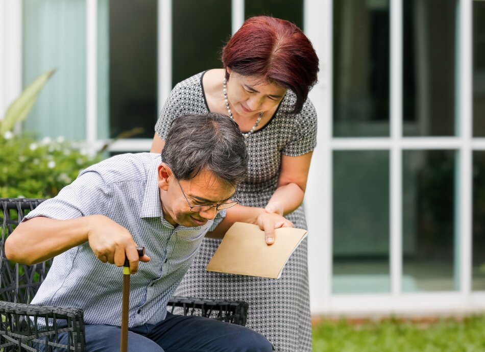 Older man with stick being helped from up chair by carer