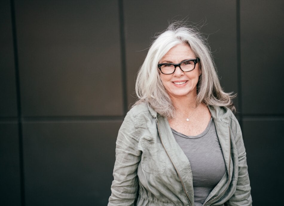 Woman in her 60s with greying hair and wearing glasses